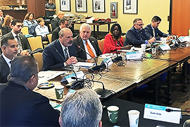 Secretary Scott sitting with a group of individuals at a desk with a microphone placed in front of each of them. 