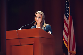 Secretary Hughs standing behind a podium with the U.S. flag in the background.